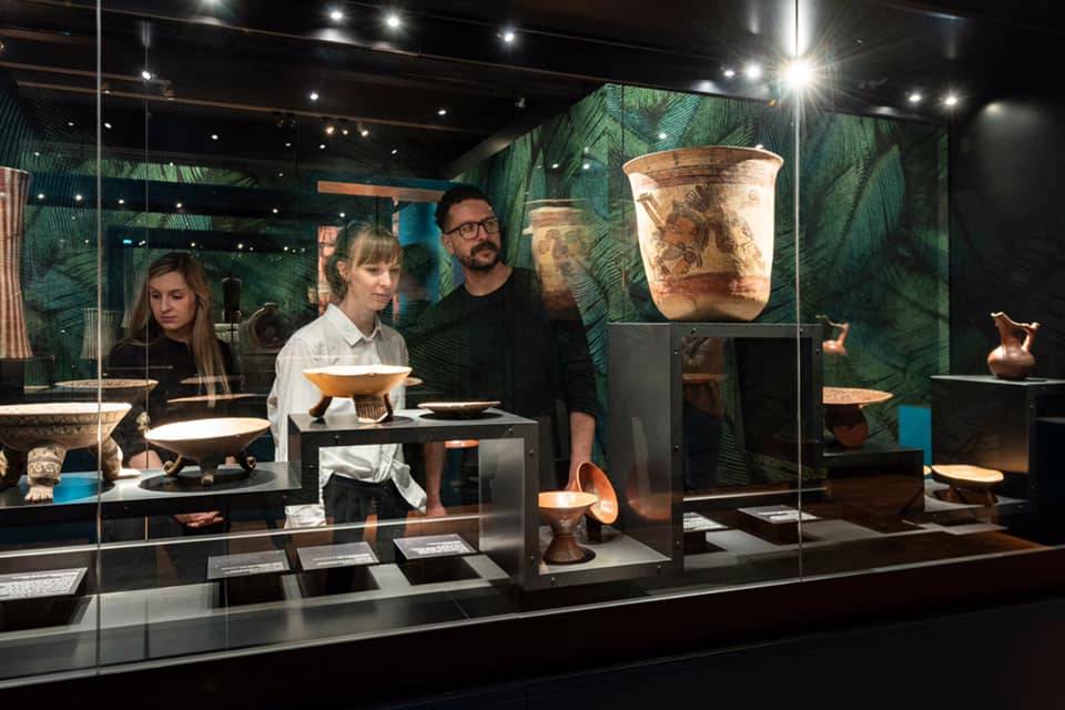 Zwei Frauen und ein Mann betrachten Objekte der Azteken in einer Vitrine