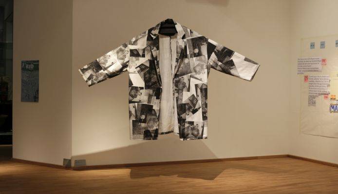 Ein Mantel, bedruckt mit schwarz-weißen Fotos, ist von der Decke abgehängt