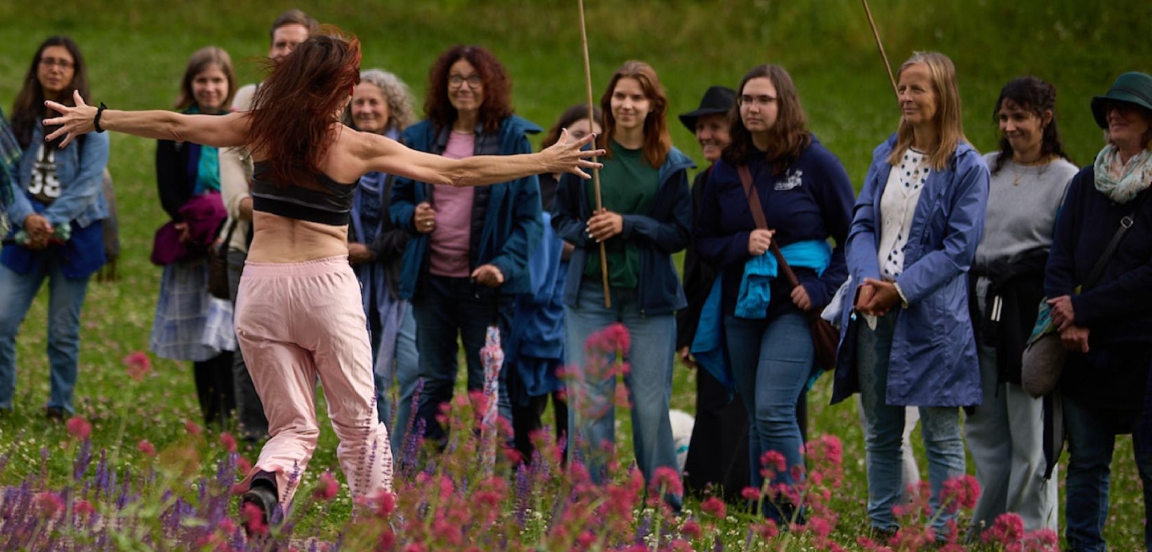 Erzählerin mit langen schwarzen Haaren und ausgebreiteten Armen auf einer Blumenwiese vor Publikum