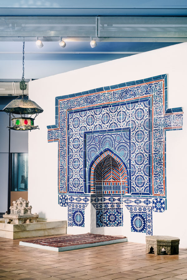 Blick in die Dauerausstellung "Orient". Im ersten Ausstellungsraum befinden sich eine marokkanische Moscheelampe, eine geflieste pakistanische Qibla-Wand mit Mihrab, ein Gebetsteppich aus Turkestan, eine Fußwaschbank aus Pandschab und ein osmanischer Brunneneinsatz