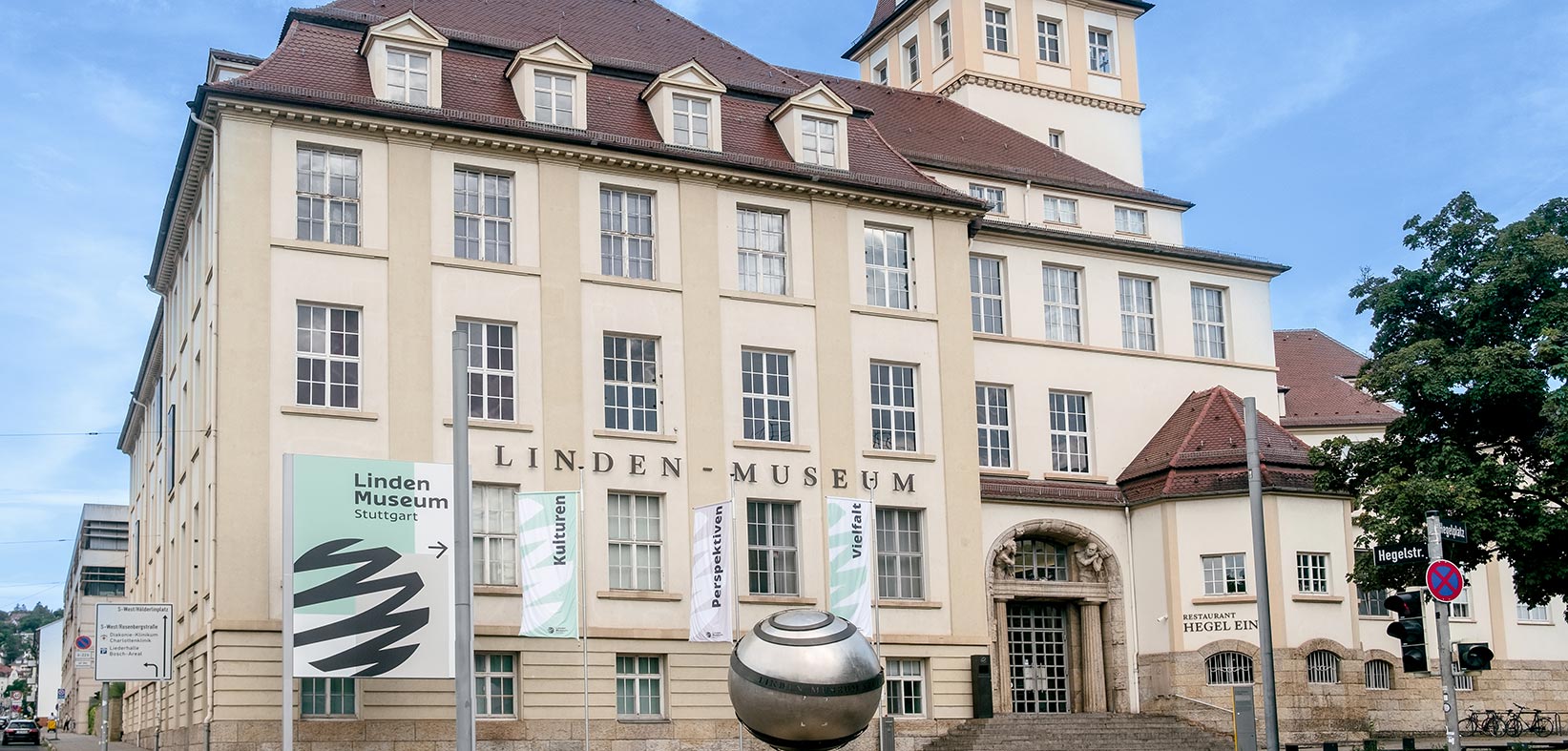 Museum von außen: 3-stöckiges Gebäude im Historismus-Stil mit Turm, Kugelskulptur und Fahnen auf dem Vorplatz
