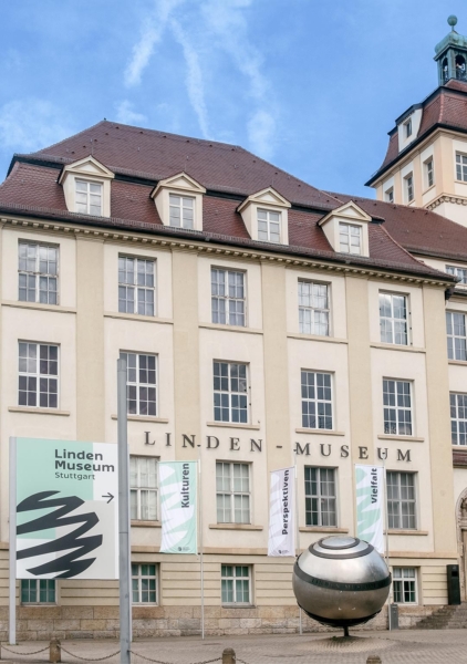 Museum von außen: 3-stöckiges Gebäude im Historismus-Stil mit Turm, Kugelskulptur und Fahnen auf dem Vorplatz